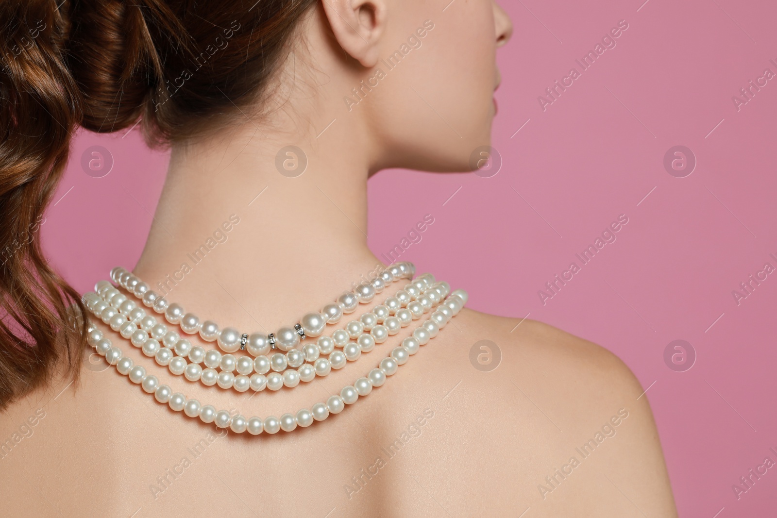 Photo of Young woman wearing elegant pearl necklace on pink background, back view