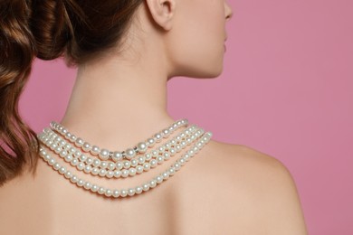 Photo of Young woman wearing elegant pearl necklace on pink background, back view
