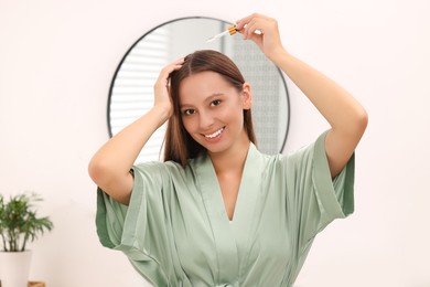 Photo of Beautiful woman applying serum onto hair indoors