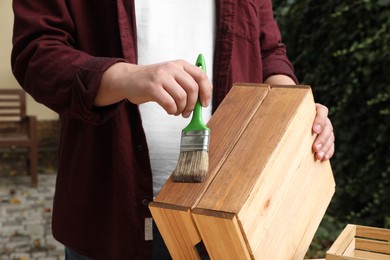 Photo of Man applying wood stain onto crate outdoors, closeup