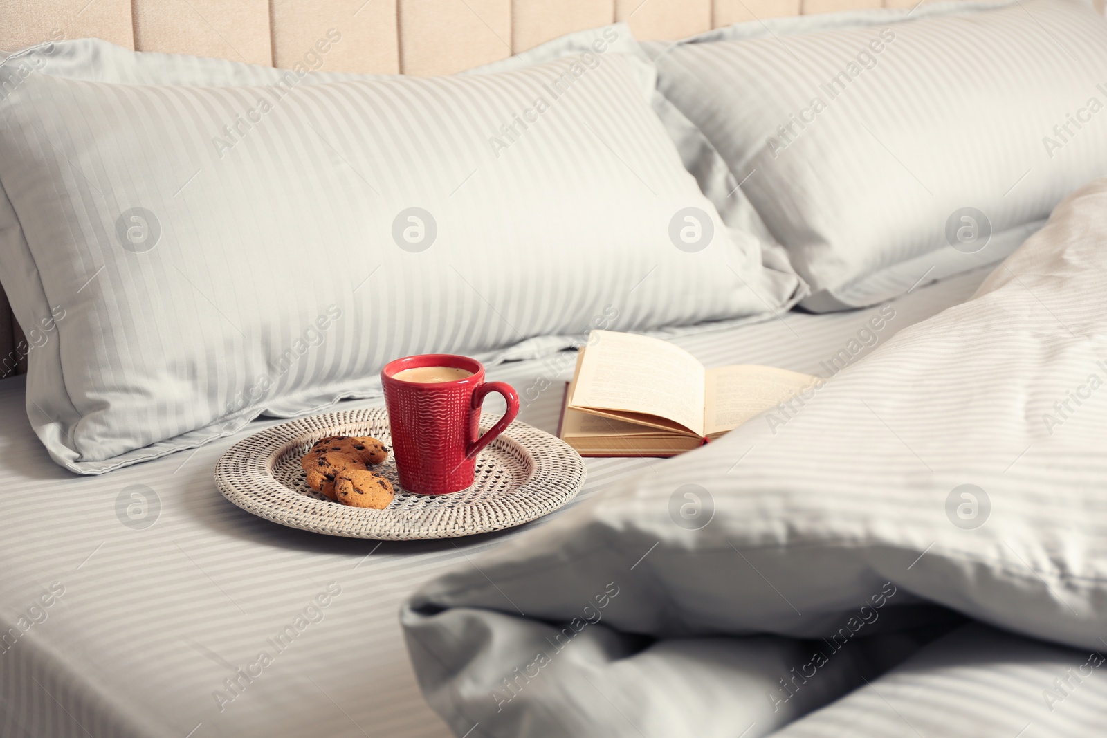 Photo of Cup of aromatic coffee, cookies and book on bed with soft blanket