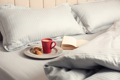 Cup of aromatic coffee, cookies and book on bed with soft blanket