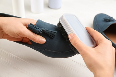 Woman taking care of stylish shoe at white table, closeup