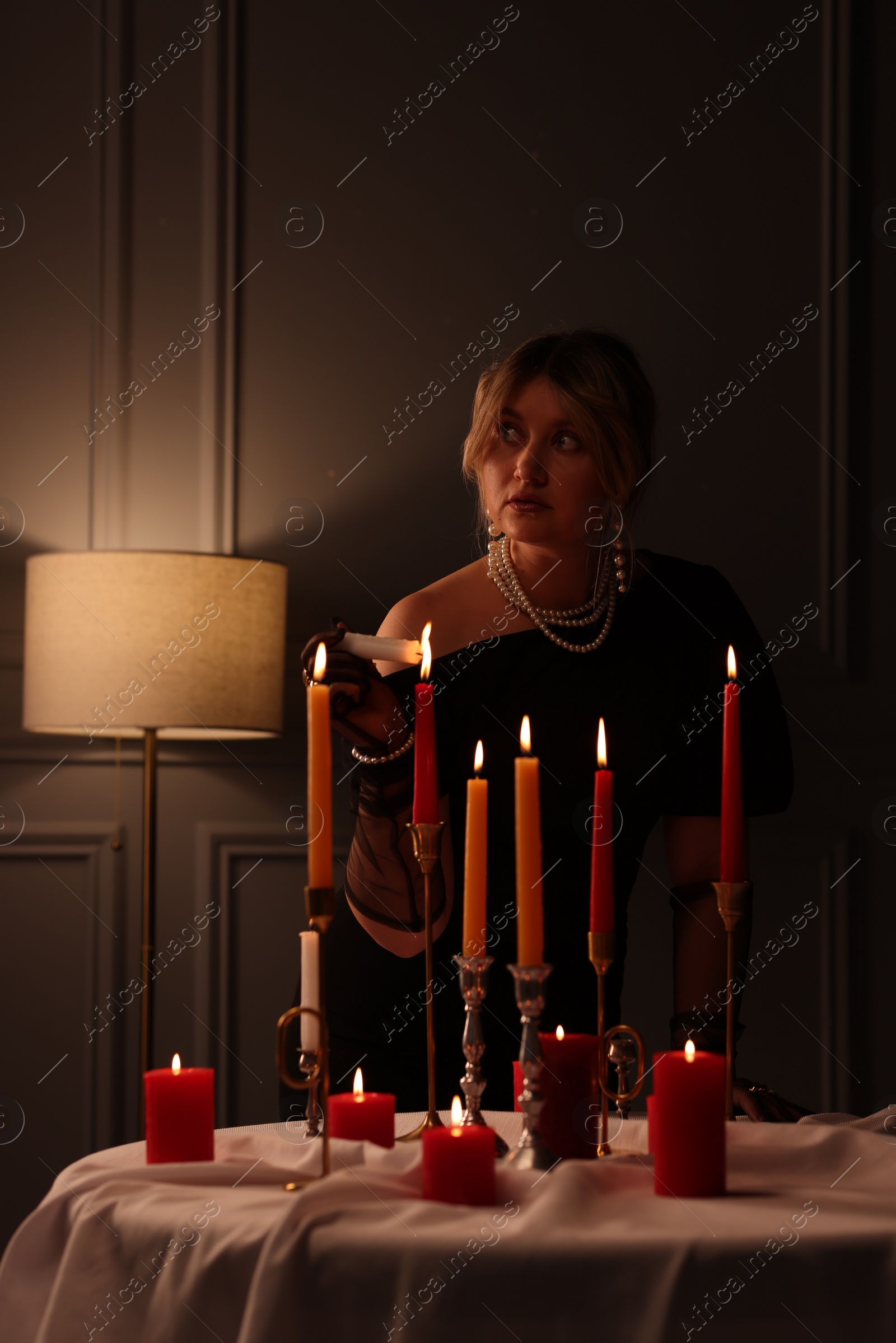 Photo of Beautiful young woman lightning up candle at table indoors