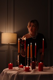 Beautiful young woman lightning up candle at table indoors