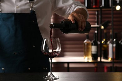 Bartender pouring red wine into glass at counter indoors, closeup