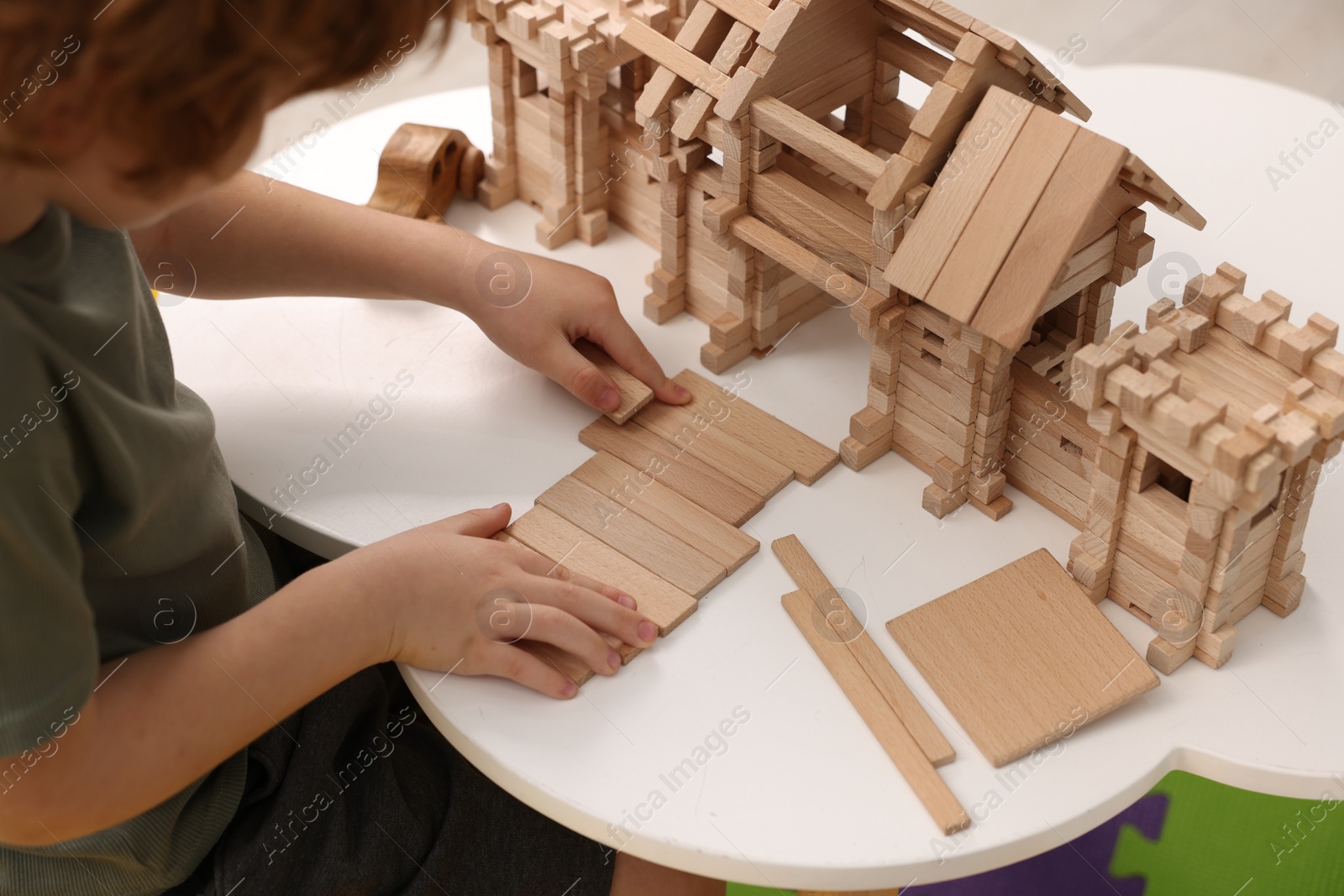 Photo of Little boy playing with wooden entry gate at white table in room, closeup. Child's toy