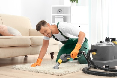 Photo of Male janitor removing dirt from rug with carpet cleaner in room