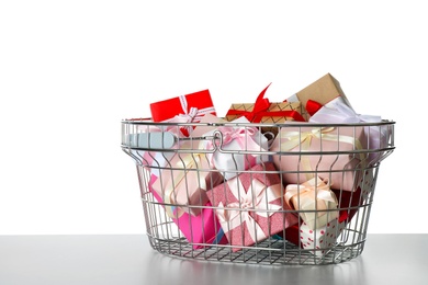 Shopping basket full of gift boxes on light grey table against white background