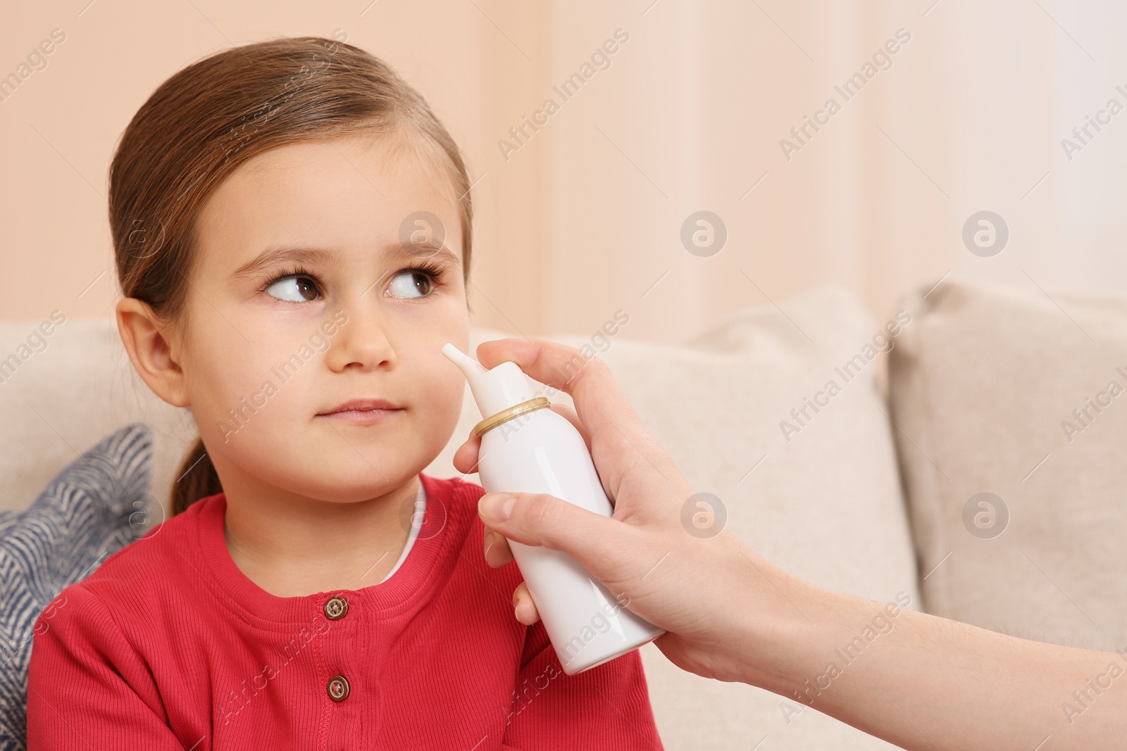 Photo of Mother using nasal spray to treat her little daughter on sofa indoors, closeup