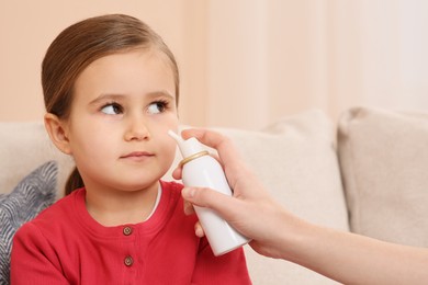 Photo of Mother using nasal spray to treat her little daughter on sofa indoors, closeup