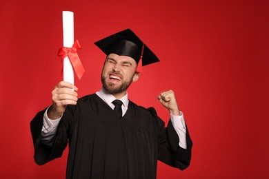Photo of Emotional student with graduation hat and diploma on red background. Space for text