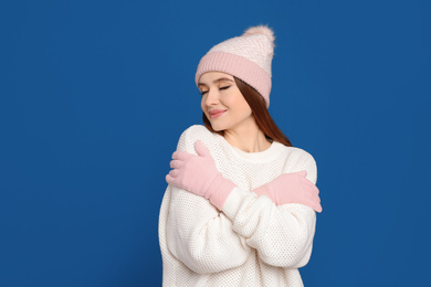 Photo of Young woman wearing warm sweater, gloves and hat on blue background. Winter season