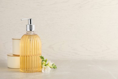 Photo of Stylish soap dispenser, flower and jars on light table. Space for text