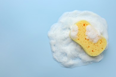 Yellow sponge with foam on light blue background, top view. Space for text