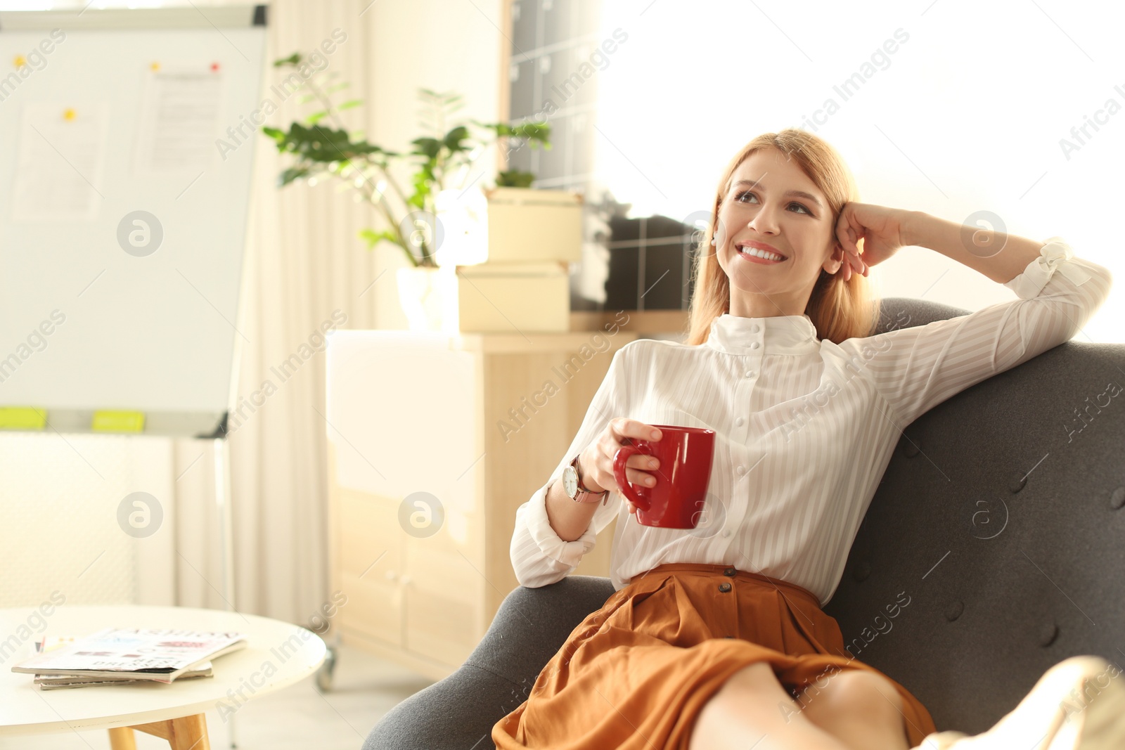 Photo of Young woman with cup of drink relaxing on couch at workplace