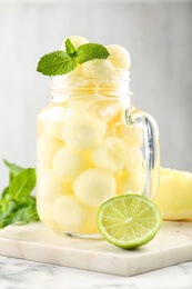 Mason jar of melon ball cocktail served with mint and lime on white marble table