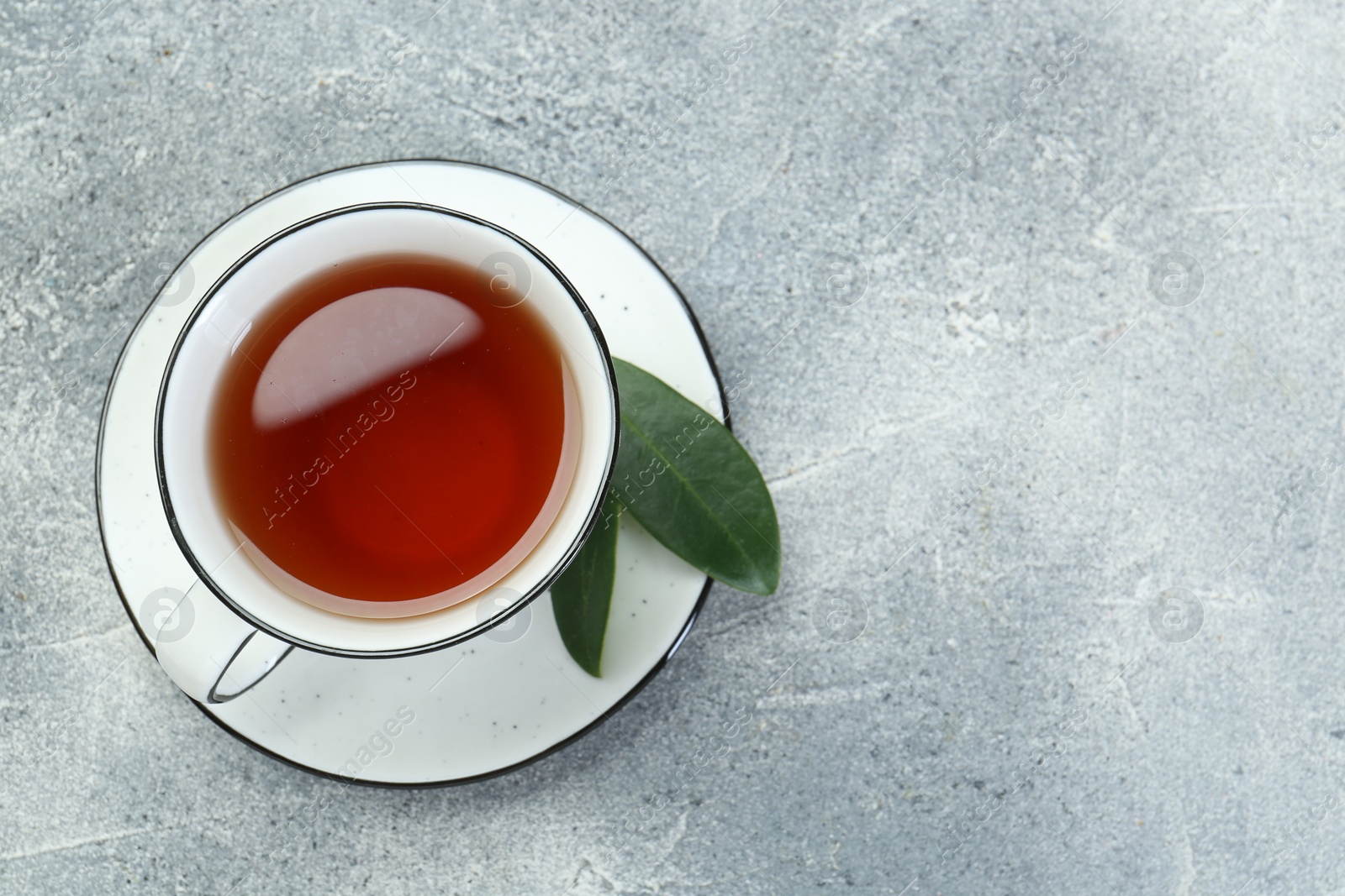 Photo of Aromatic tea in cup and green leaves on grey table, top view. Space for text