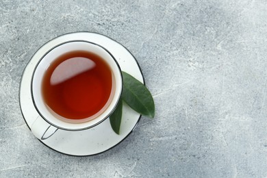 Aromatic tea in cup and green leaves on grey table, top view. Space for text