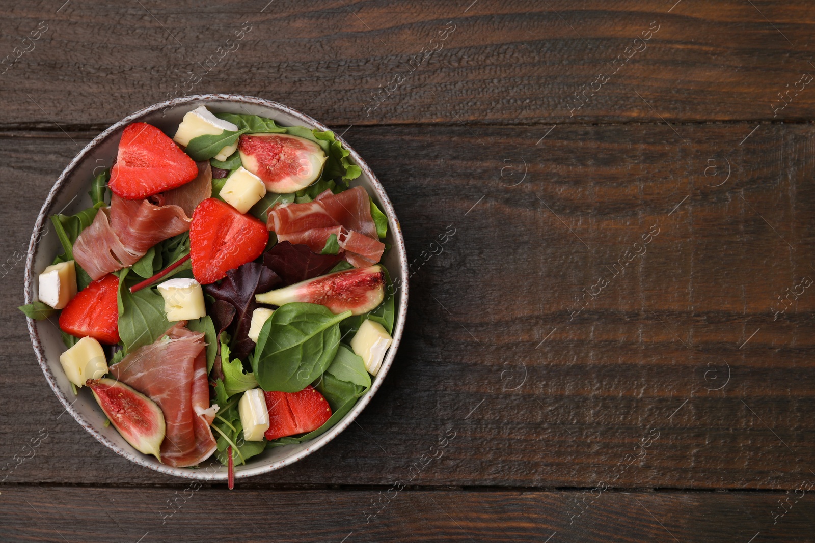 Photo of Tasty salad with brie cheese, prosciutto, strawberries and figs on wooden table, top view. Space for text