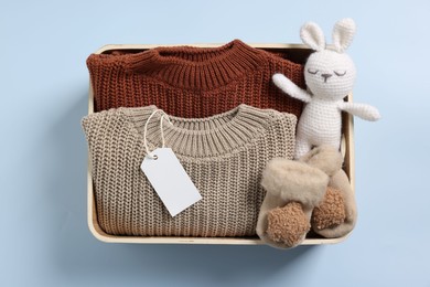 Different baby accessories, knitted sweaters and blank card in box on light blue background, top view
