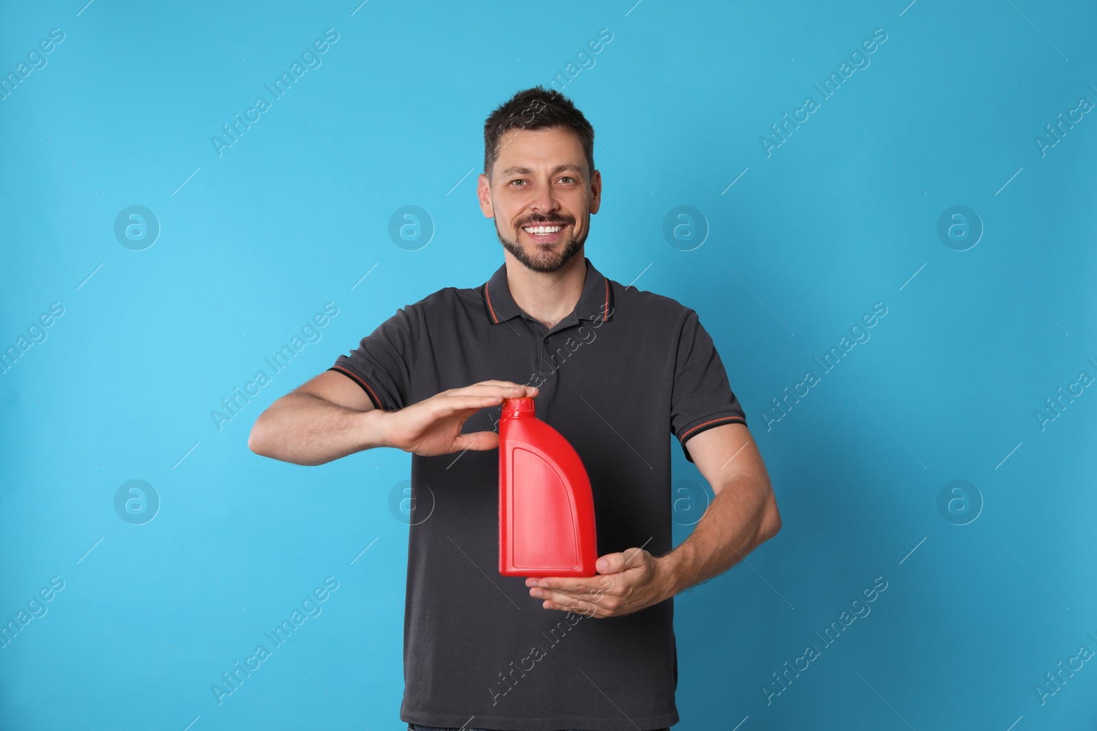 Photo of Man holding red container of motor oil on light blue background