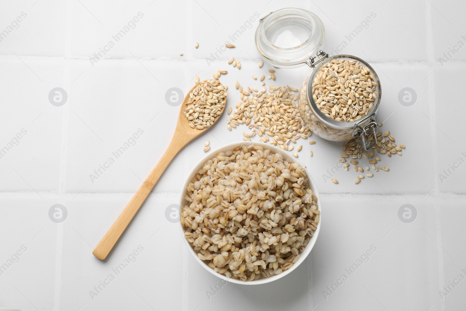 Photo of Delicious pearl barley served on white tiled table, flat lay