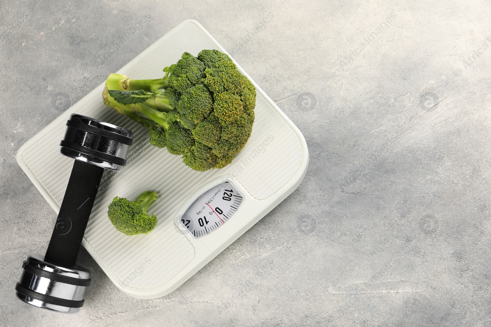 Photo of Healthy diet. Scale, broccoli and dumbbell on grey table, top view. Space for text