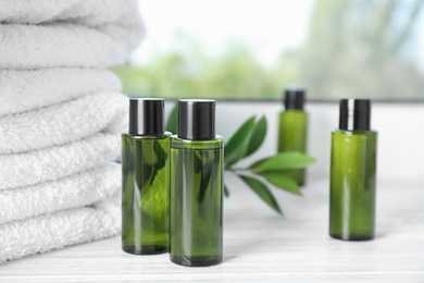 Photo of Mini bottles with cosmetic products and towels on white wooden window sill