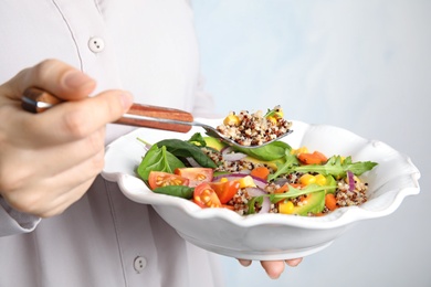 Photo of Woman eating healthy quinoa salad with vegetables from plate, closeup