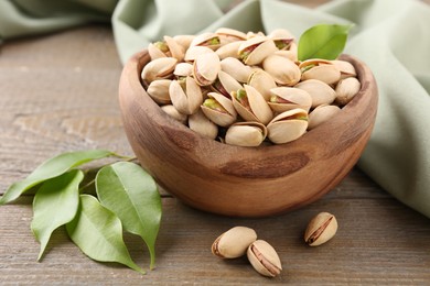 Photo of Delicious pistachios in bowl on wooden table, closeup