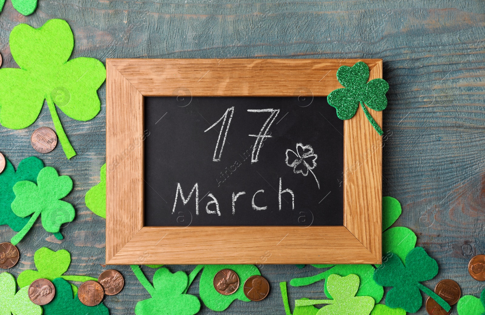 Photo of Chalkboard with written 17 March, clover leaves and gold coins on blue wooden background. St. Patrick's Day celebration