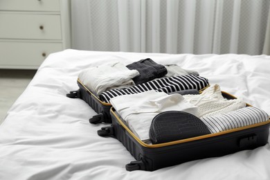 Open suitcase with clothes on bed indoors