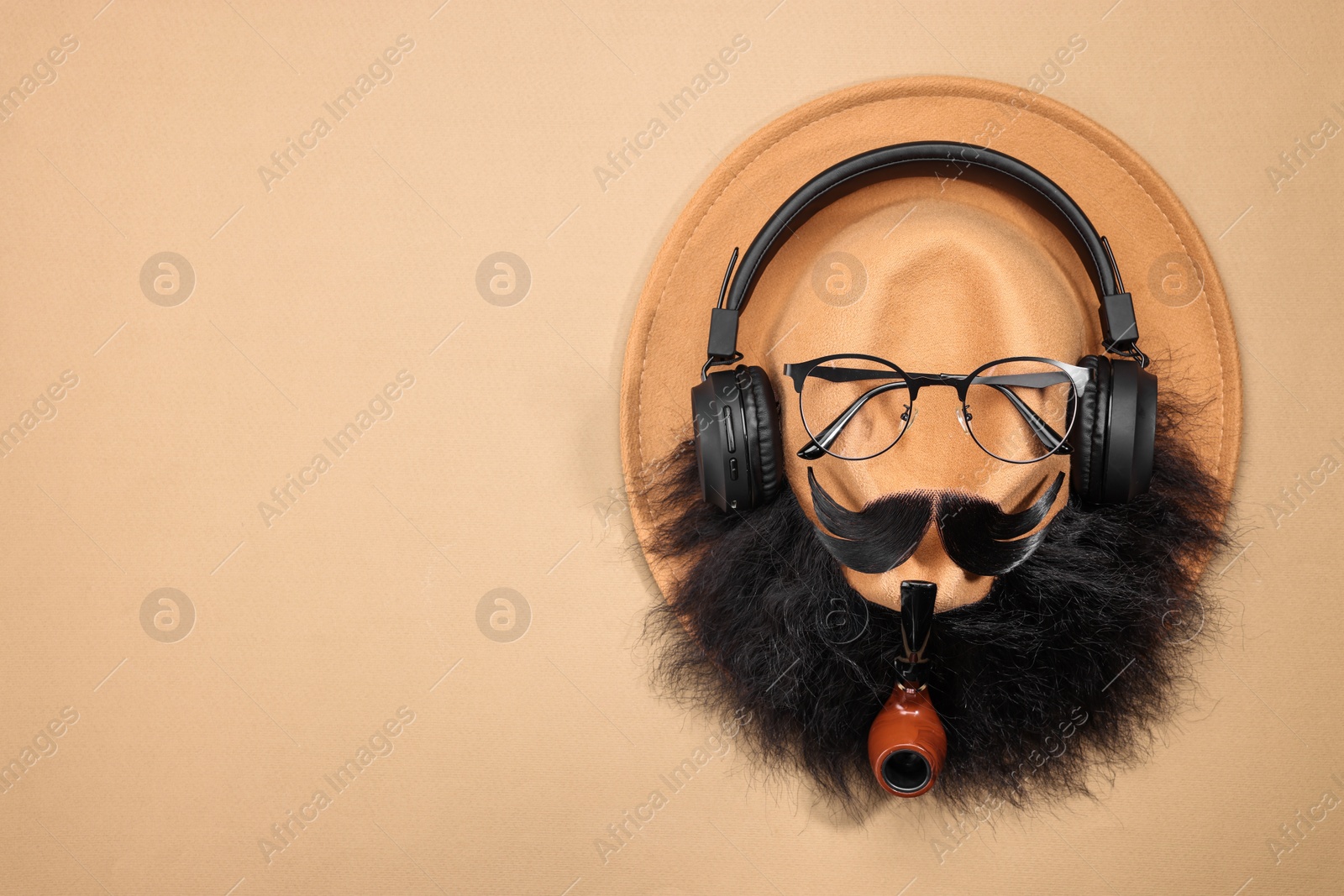 Photo of Man's face made of artificial mustache, beard, glasses and hat on beige background, top view. Space for text