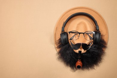 Photo of Man's face made of artificial mustache, beard, glasses and hat on beige background, top view. Space for text