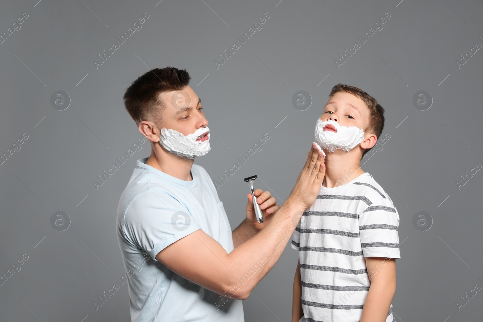 Photo of Dad applying shaving foam on son's face, grey background