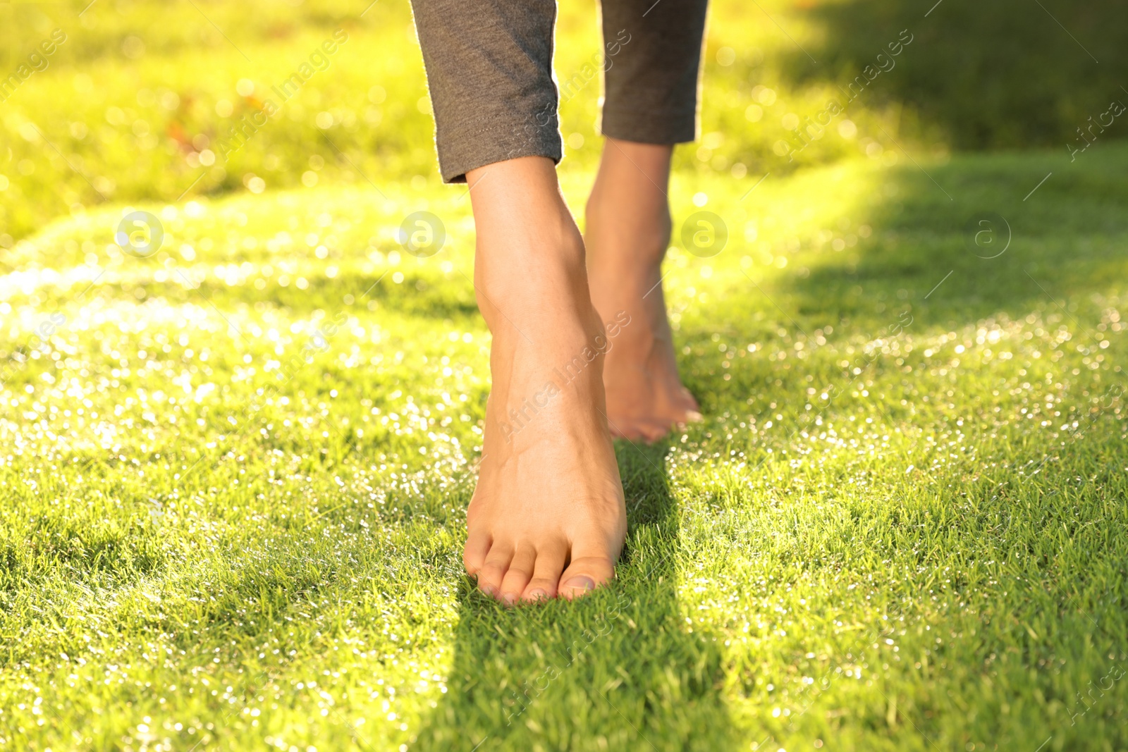 Photo of Young woman walking barefoot on fresh green grass, closeup