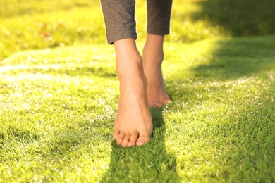 Young woman walking barefoot on fresh green grass, closeup