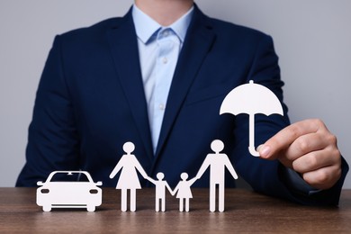 Photo of Man holding figure of umbrella near family and car at wooden table. closeup. Insurance concept