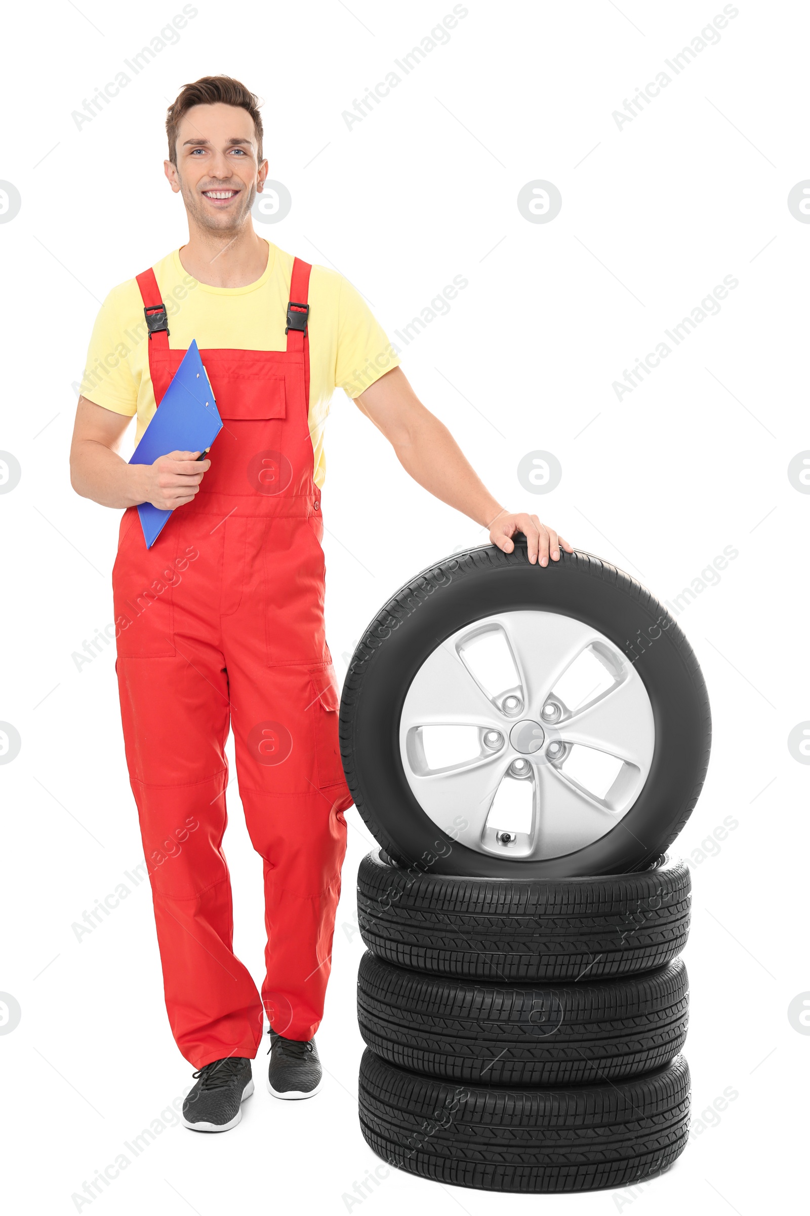 Photo of Young auto mechanic with clipboard and car tires on white background