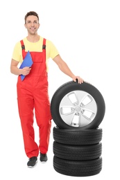 Photo of Young auto mechanic with clipboard and car tires on white background