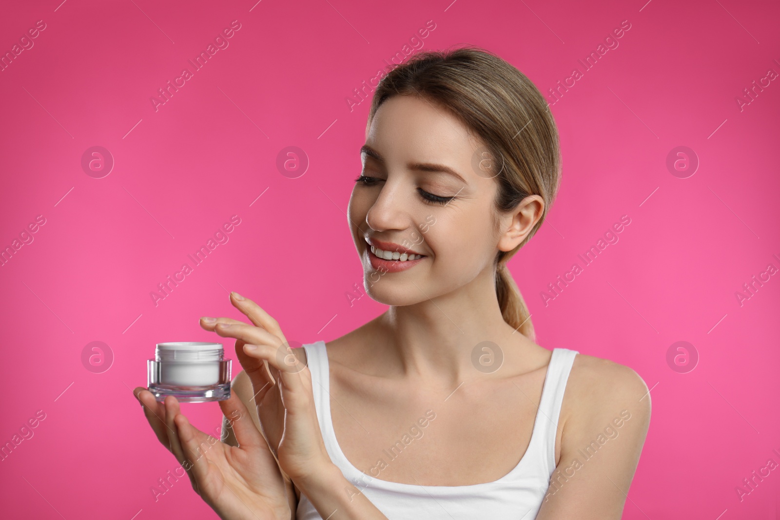 Photo of Young woman holding jar of facial cream on pink background