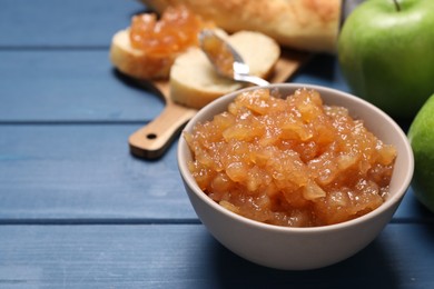 Photo of Bowl with delicious apple jam on blue wooden table, space for text