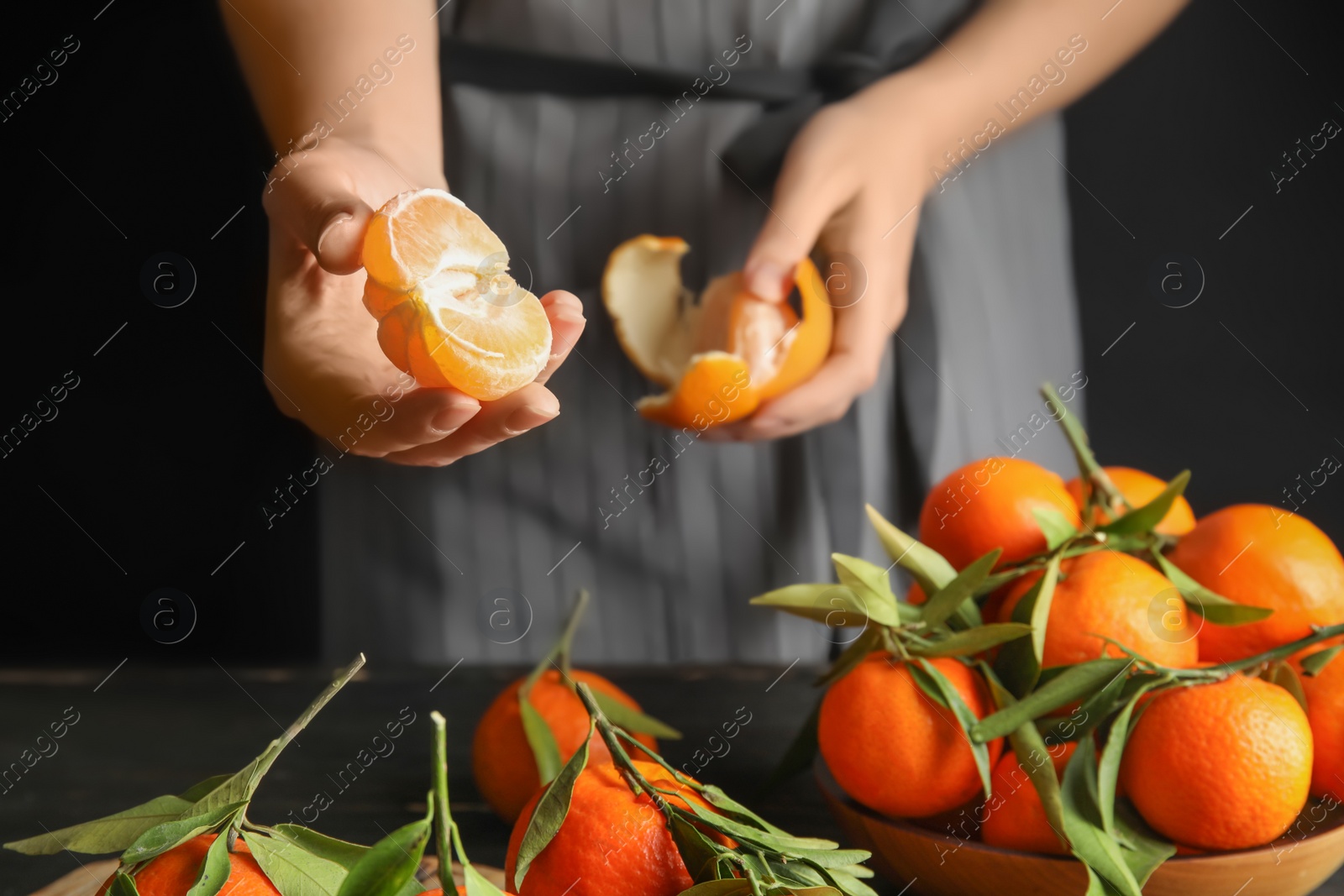 Photo of Woman peeling ripe tangerine over table on dark background, closeup