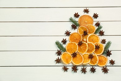 Photo of Flat lay composition with dry orange slices, fir branches and anise stars arranged in shape of Christmas tree on white wooden table. Space for text