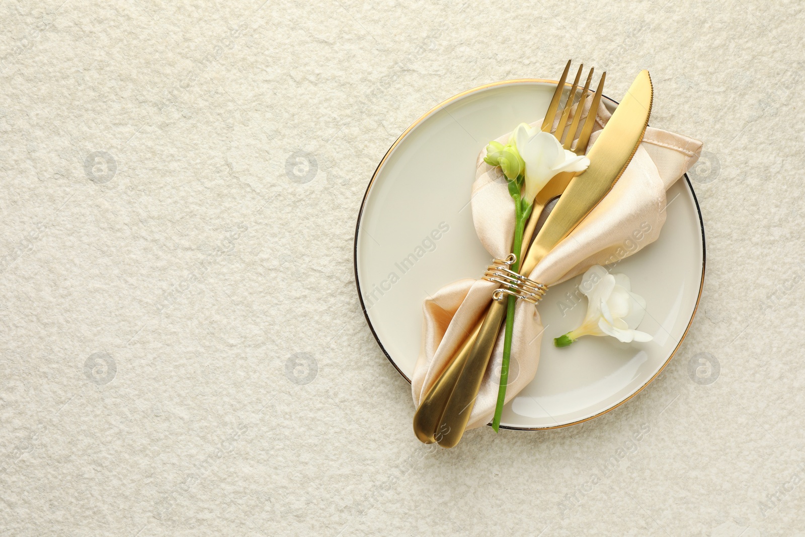 Photo of Stylish setting with cutlery, napkin, flowers and plate on light textured table, top view. Space for text