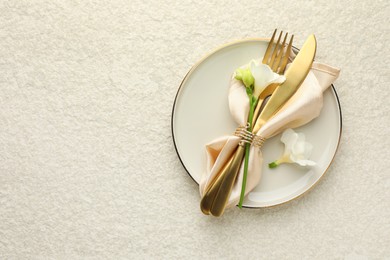 Stylish setting with cutlery, napkin, flowers and plate on light textured table, top view. Space for text