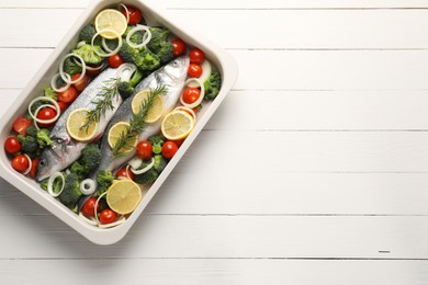 Photo of Raw fish with vegetables and lemon in baking dish on white wooden table, top view. Space for text