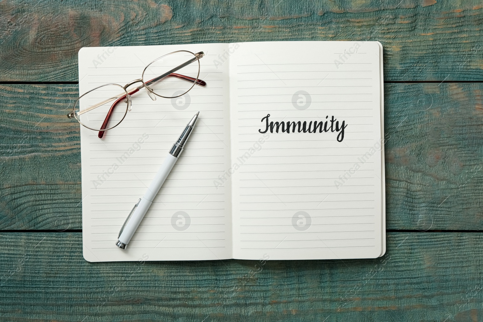 Photo of Notebook with word Immunity, glasses and pen on blue wooden table, top view