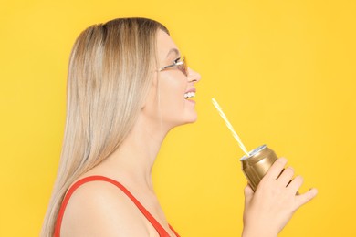 Photo of Beautiful happy woman drinking from beverage can on yellow background